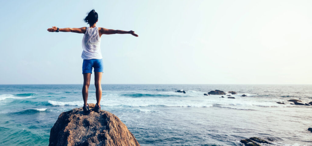 אישה על קצה צוק מול הים - להעיז ולא לפחד עפ תמצית אספן