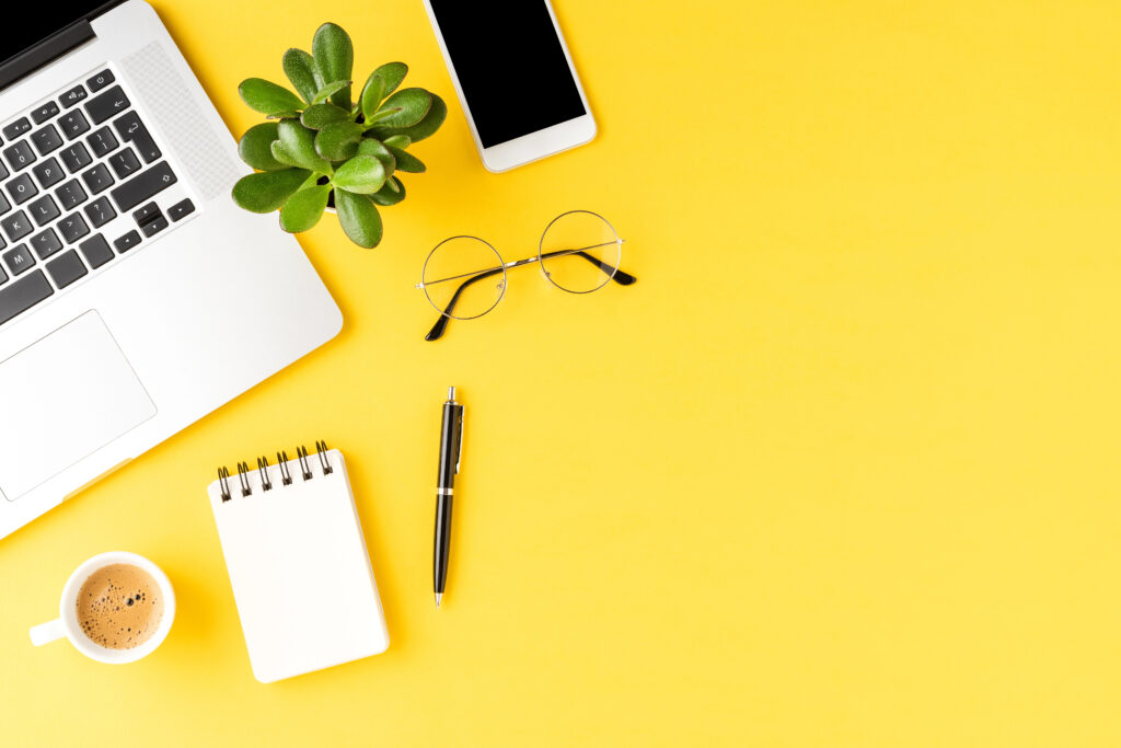 מחשב, טלפון ומשקפי קריאה על שולחן צהוב - חוסן ארגוני מתחיל ברווחת העובד